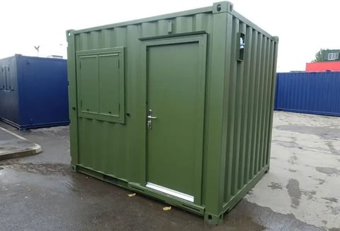 Green shipping container with double doors in an industrial yard setting with other containers in background